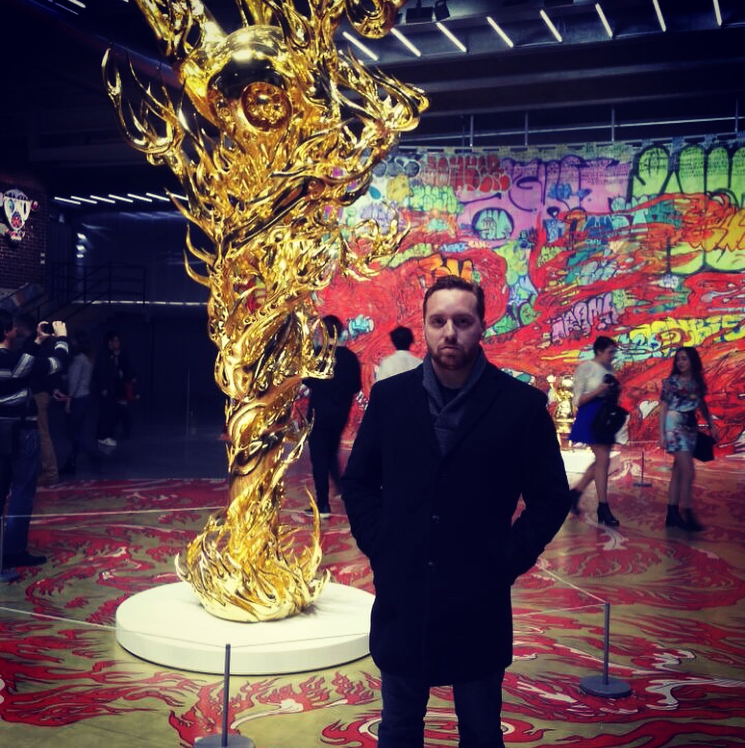 Standing beside a twisting gold sculpture in a vividly colored art gallery.